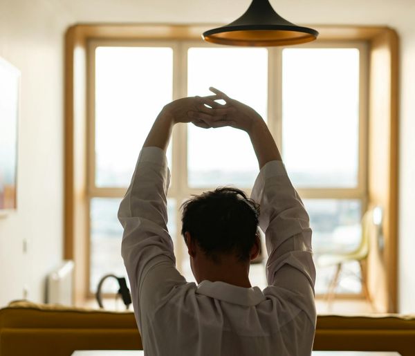 A person stretching in a spacious, well-lit room with large windows.